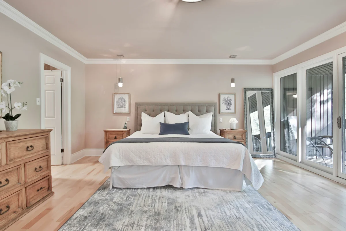 Bright master bedroom with a tufted gray headboard, white bedding, and two wooden nightstands on either side of the bed.
